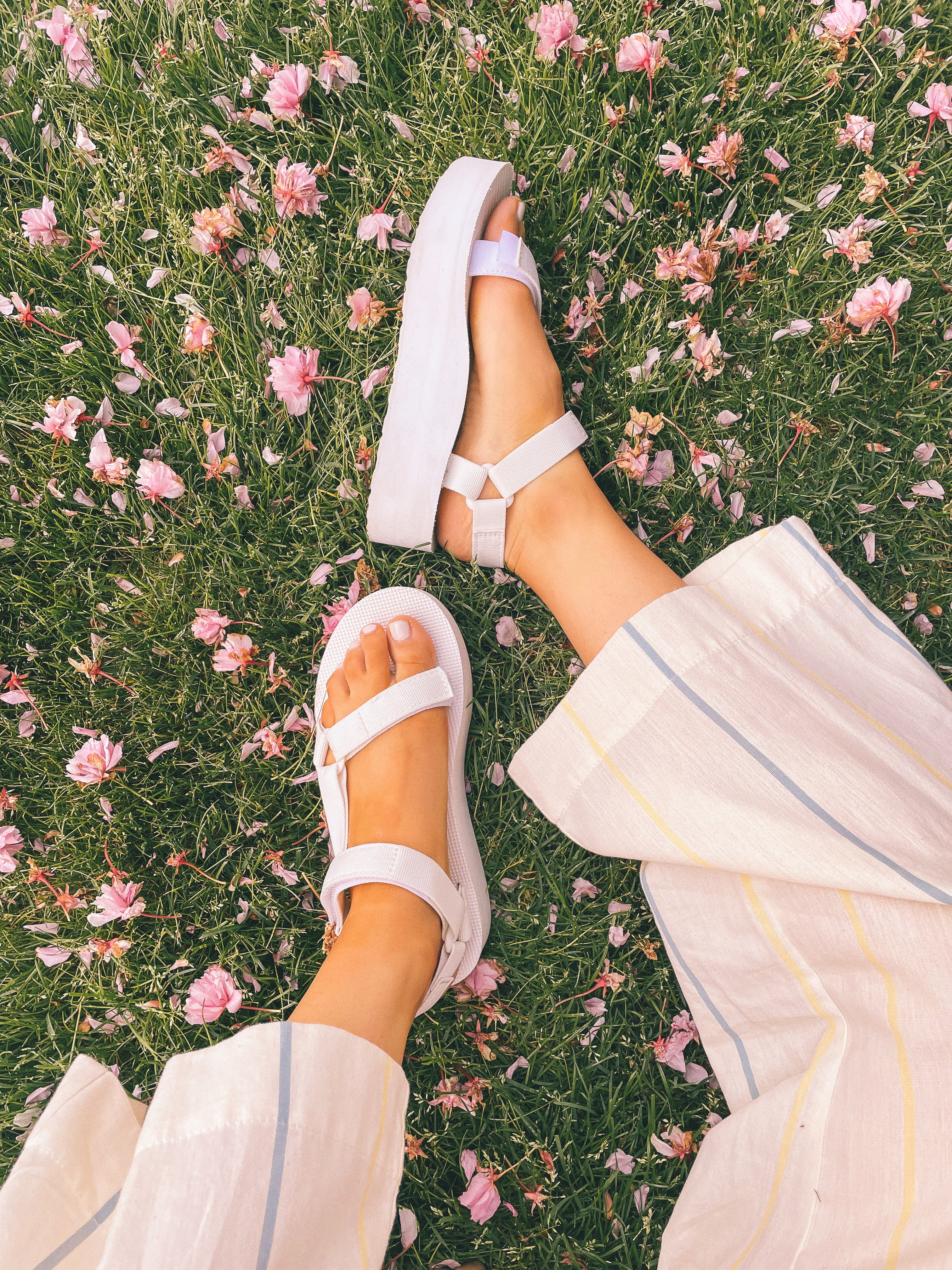 Platform white Teva sandals paired with striped pants in a field of flowers