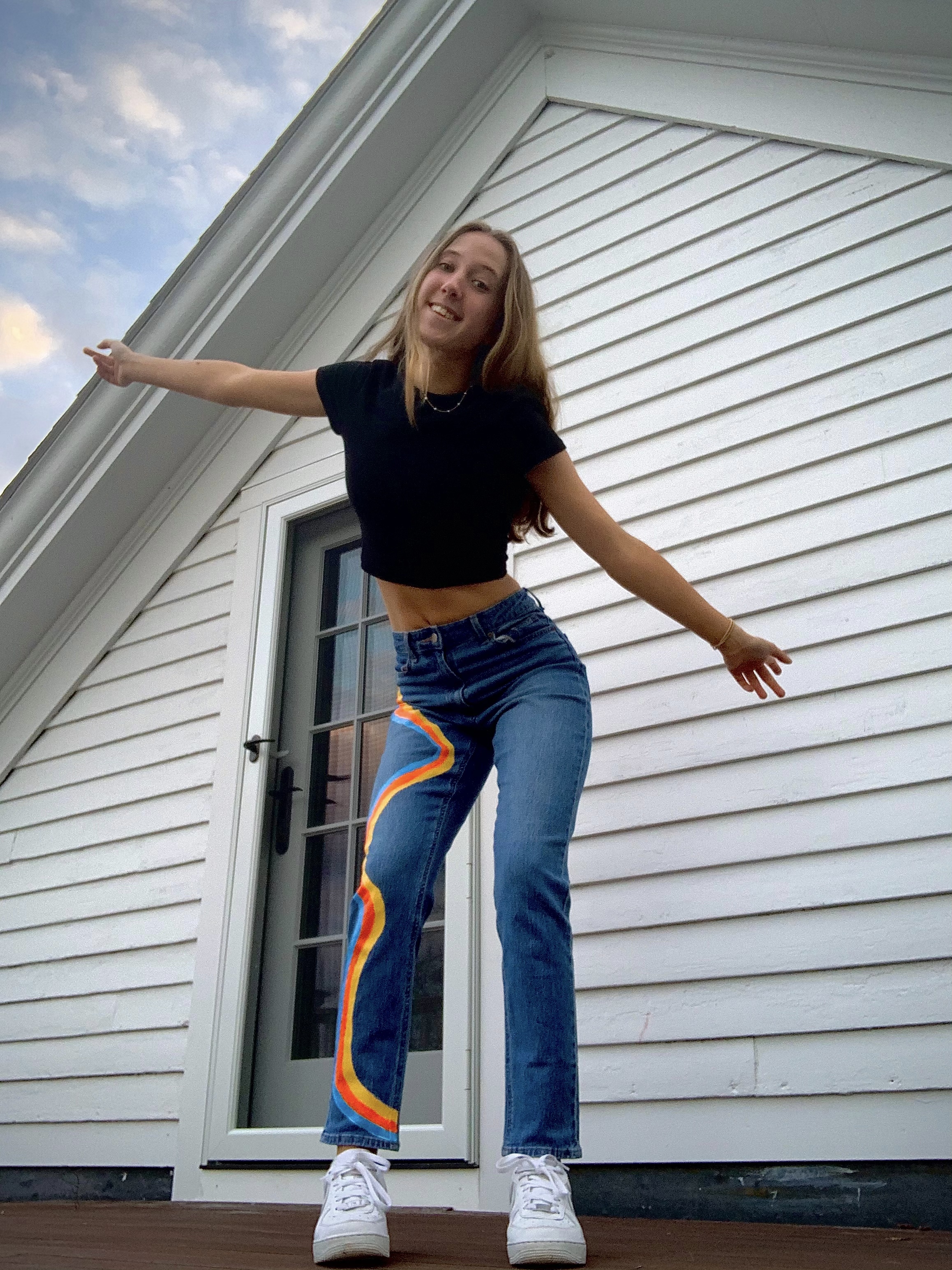 Girl in black t-shirt and jeans with yellow, orange, and blue stripes.